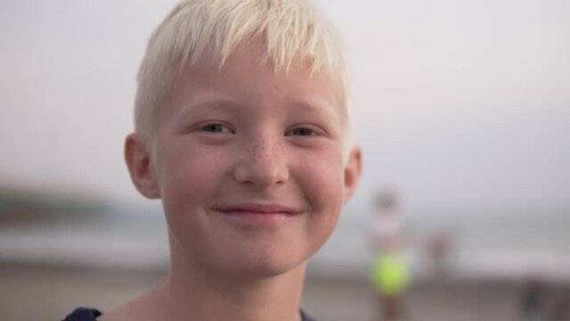 Close-up of the face of a beautiful tanned teenager boy with freckles against the background of the washed-up sea and beach.