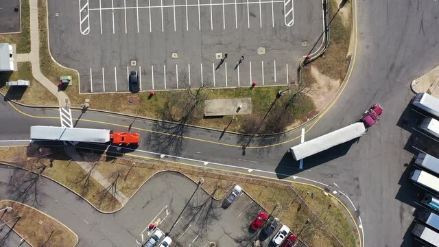 A top down shot over two trucks pulling in to a truck stop on a sunny day. The drone camera, pointing straight down, truck right following them as they prepare to park.