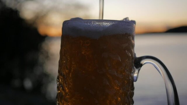 As the sun sets on the Swedish archipelago a cold lager beer is poured in to a rippled beer glass in slow motion. Vibrant colors and great depth of field helps to enhance the stunning seaside setting.