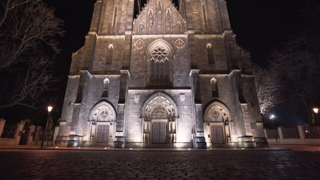 The illuminated entrance and front side of the gothic stone medieval church of saint Peter and Paul with its two spires at Vy&scaron;ehrad,Prague,Czechia,at night,on an empty paved square with lanterns,tilt.