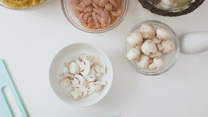 Bowl of fresh raw organic mushrooms and bowl of chopped chicken fillet close up on white background.
