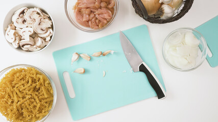 Garlic gloves close up on cutting board on white kitchen table, flat lay, copy space. Ingredients for pasta with chicken and mushrooms recipe