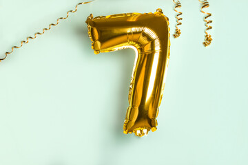 Decoration for seven birthday party. Golden balloon in form of 7 number on blue background.