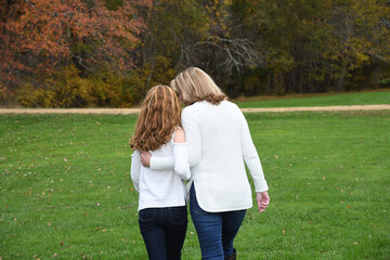 Two ladies, grandmother and grand daughter, walk together during autumn in the park. 