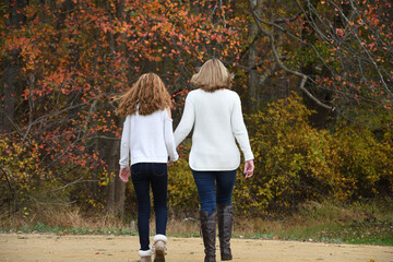 Two ladies, grandmother and grand daughter, walk together during autumn in the park. 