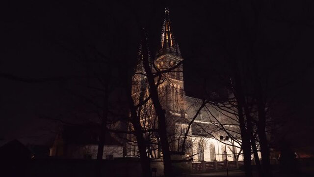 The illuminated gothic medieval church of saint Peter and Paul with its two spires at Vy&scaron;ehrad,Prague,Czechia,at night,shot through the silhouettes of leafless tree branches,looking dark and ominous.