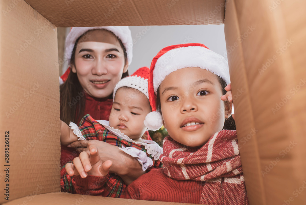 Wall mural merry christmas and happy holidays. parent and two little children opening a christmas present. little kid having fun near christmas tree indoors. view from inside of the box. child playing at home