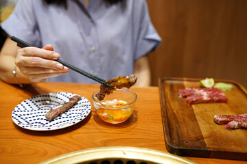 Hand holding chopsticks to pick grilled wagyu beef and dip into pickled egg yolk sauce, Traditional Japenese food.