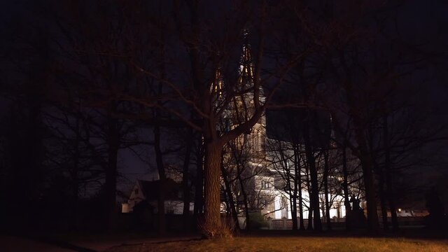 The illuminated gothic medieval church of saint Peter and Paul with its two spires at Vy&scaron;ehrad,Prague,Czechia,at night,behind a forest of leafless trees and their branches,looking scary in the dark.