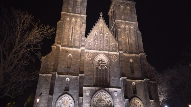 The illuminated gothic medieval church of saint Peter and Paul with its two spires at Vy&scaron;ehrad,Prague,Czechia,at night,on a small empty paved square with leafless trees on its sides, tilt shot.