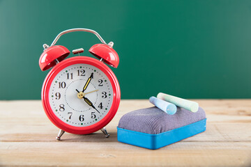 A red alarm clock and a blackboard eraser and chalk in front of the teaching blackboard
