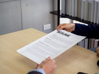 Fototapeta premium Resume or CV paper. Applicant's hand giving resume to employer for review the profile of the applicant.