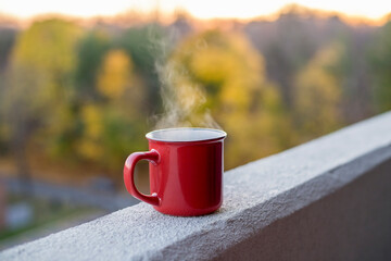 Cup of hot drink standing on the edge of balcony in high building  with  blurred trees in the background