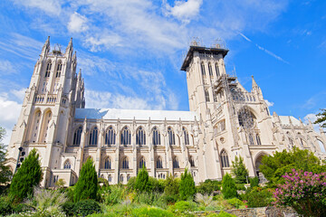 National Cathedral and gardens of Washington DC, USA. Gothic building surrounded by gardens under blue sky with cloud on a sunny day in spring. - 389533049