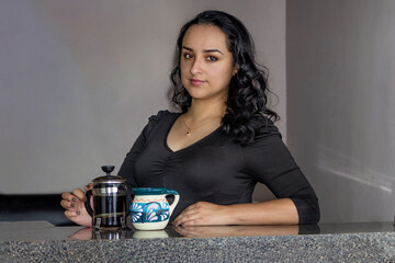 Beautiful Mexican woman showing coffee from a French press next to Mexican mug