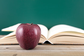 An open book and a red apple in front of the blackboard