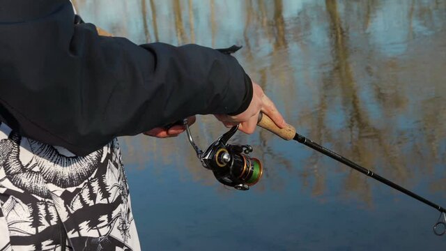 Hands of a man in a jacket holding a fishing rod and fishing on the river bank