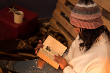 Above photography girl reading a book wears winter hat and white sweater on a cold night.