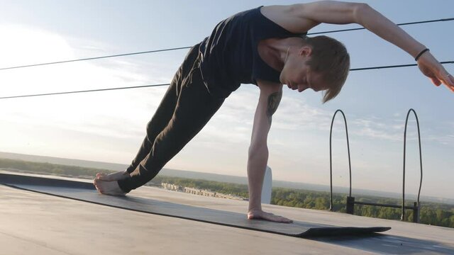 a young and strong Caucasian type yogi performs several assanas in a row on the roof with sunrise. Yoga in the morning outdoors. 4k