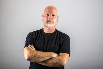 Grumpy old man with his arms crossed and stern expression on his gray beard covered face