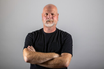 portrait of an old, mature man with his arms crossed and a stern expression on bearded face