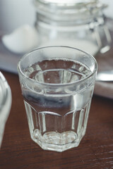 Glass of clean boiled water on the table, ingredients for making dough, for baking pancakes.