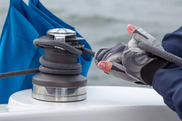 Woman hands in gloves holding the rope on sailing boat yacht sheet winch closeup on water sea...