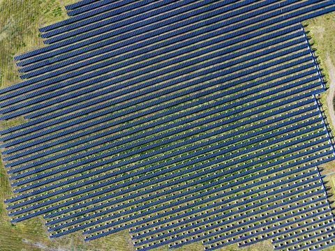 Aerial view of massive solar panel array in field from above. Drone photo looking down on rows of solar panels in field.