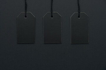 Blank black cardboard paper labels or price tags with cord isolated on dark background. Black Friday, Shopping, sale and marketing concept. Top view, flat lay, copy space. .