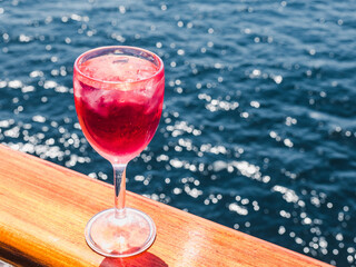 Beautiful glass with a drink on the background of sea waves and sun rays. Top view, close-up. Concept of leisure and travel
