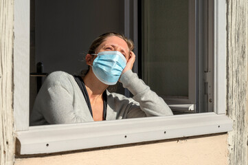 Femme triste, confinée et masquée prenant le soleil à la fenêtre ouverte de sa maison