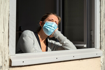 Femme triste, confinée et masquée prenant le soleil à la fenêtre ouverte de sa maison