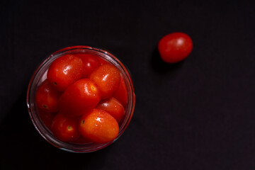 low key photo of cherry tomatoes in a glass jar isolated on black background
