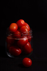 low key photo of cherry tomatoes in a glass jar isolated on black background