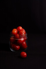 low key photo of cherry tomatoes in a glass jar isolated on black background
