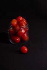 low key photo of cherry tomatoes in a glass jar isolated on black background