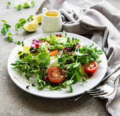 Fresh green mixed  salad bowl with tomatoes and microgreens  on  concrete background. Healthy food, top view.