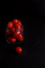 low key photo of cherry tomatoes in a glass jar isolated on black background