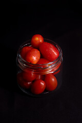 low key photo of cherry tomatoes in a glass jar isolated on black background