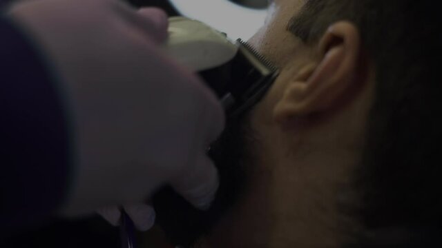 A bearded man trims his beard in a barber shop. close-up trimer haircut