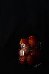 low key photo of cherry tomatoes in a glass jar isolated on black background