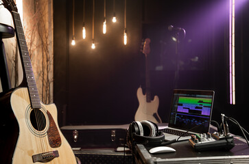 Recording studio background with acoustic guitar, laptop, sound mixer and headphones on the table. Musical creativity concept.