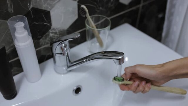Crop woman opening faucet and washing toothbrush during morning routine in bathroom at home 