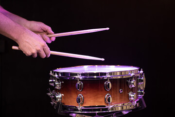 Drummer hitting drumsticks on snare drum on black background close up.