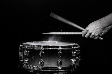 Drum sticks hitting snare drum with splashing water on black background under studio lighting....