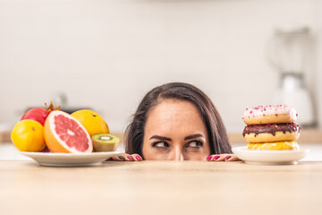 Female stares at donuts pile on a table as an opposite to a plate full of fresh fruit