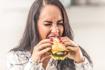 Girl trying to open her mouth as much as possible to bit off a big hamburger