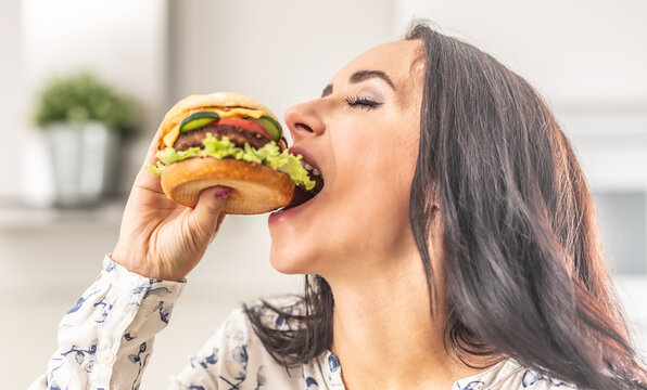Woman takes a big bite of a thick hamburger