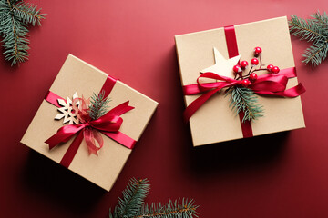 Vintage Christmas gift boxes wrapped kraft paper, wooden decorations, fir branches on marsala red background. Merry Christmas celebration concept.