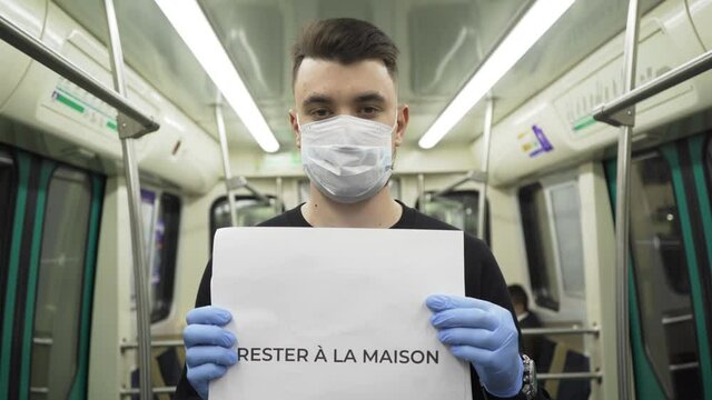 Young man in blue medical mask stand in underground carriage with "Rester &agrave; la maison" sign during pandemic covid-19 coronavirus quarantine. Keep yourself and others safety.